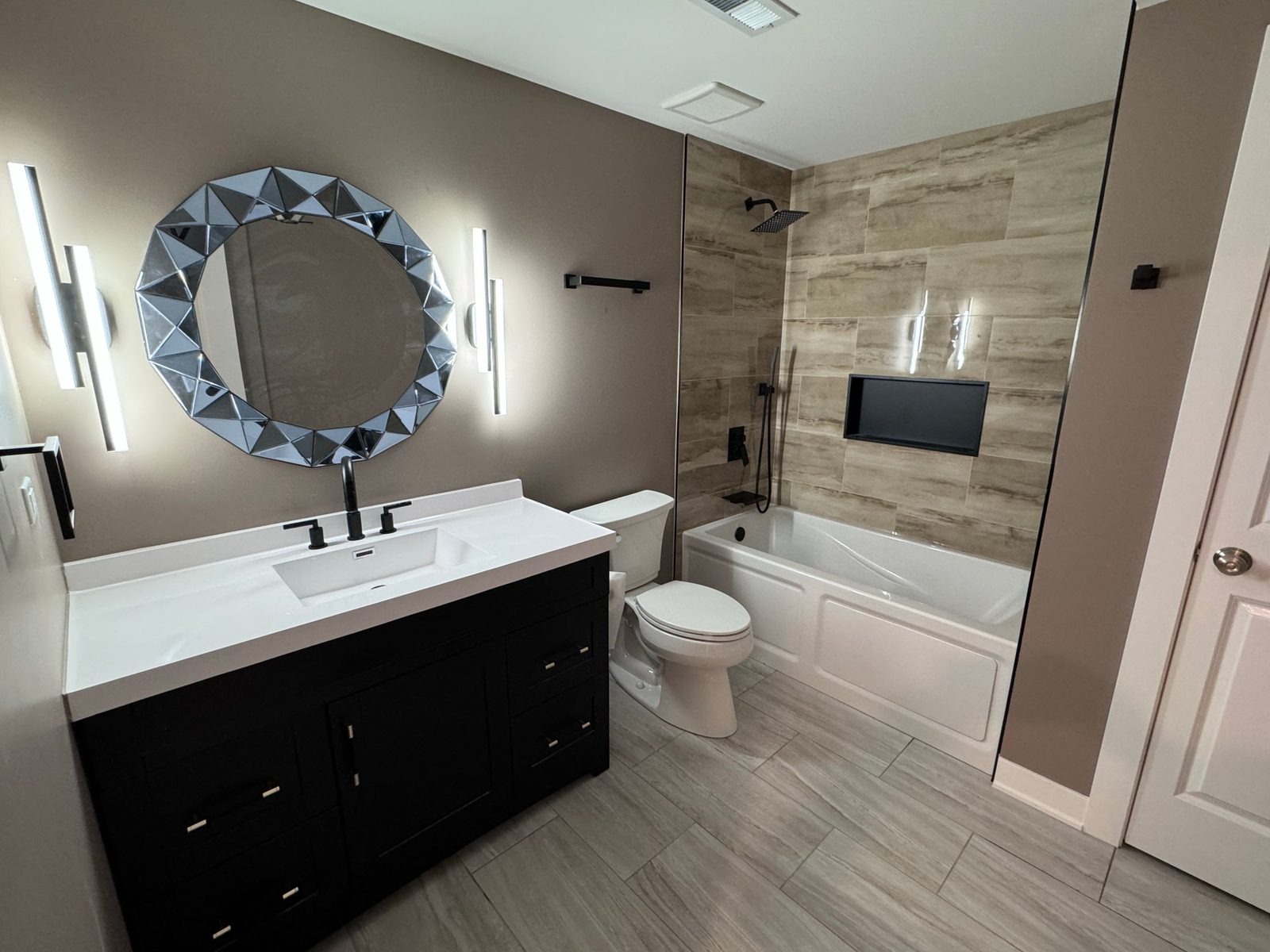 Bathroom with black vanity, geometric mirror and tiled tub surround