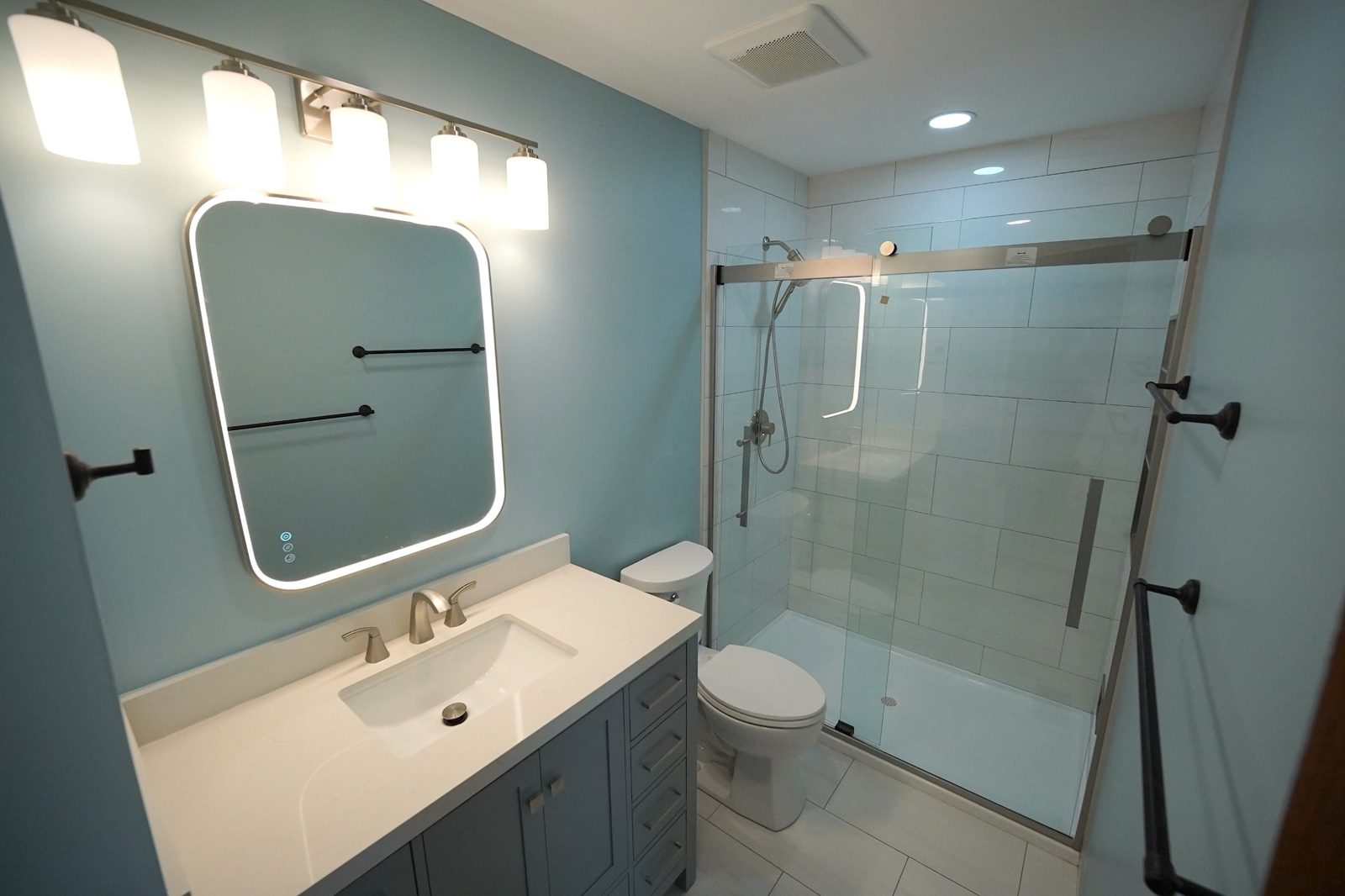 Bronze bathroom: blue walls, LED mirror, new vanity and tiled shower with glass slider door