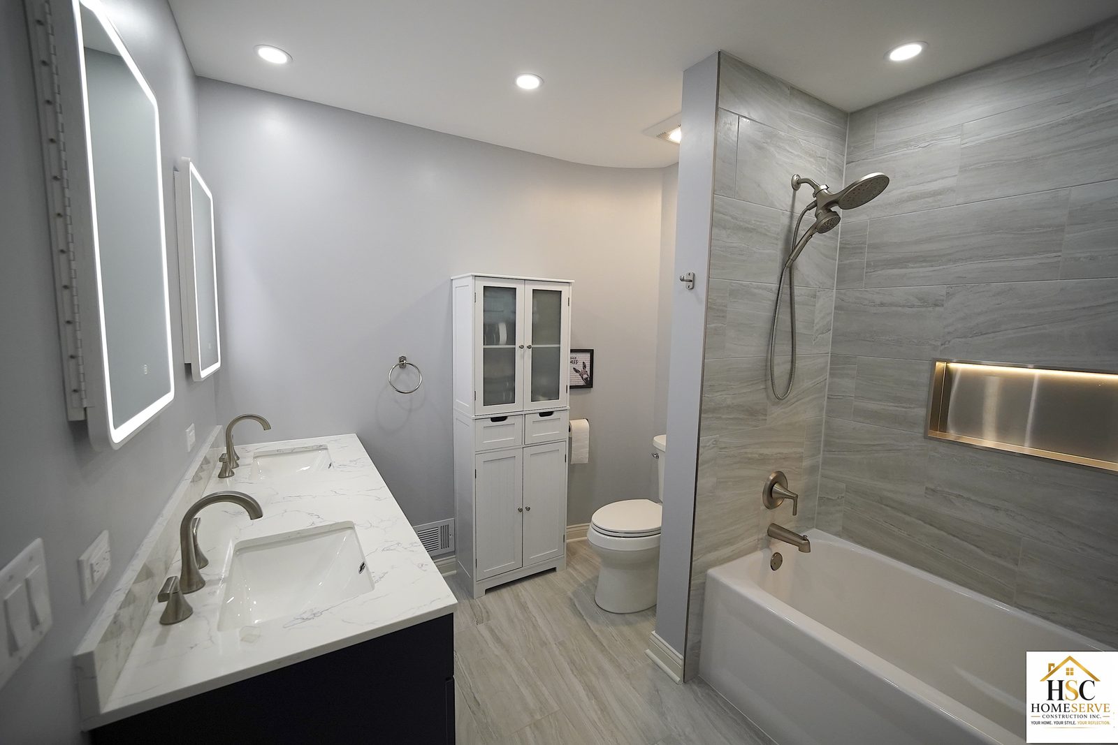 Finished bathroom with navy double vanity and tiled tub
