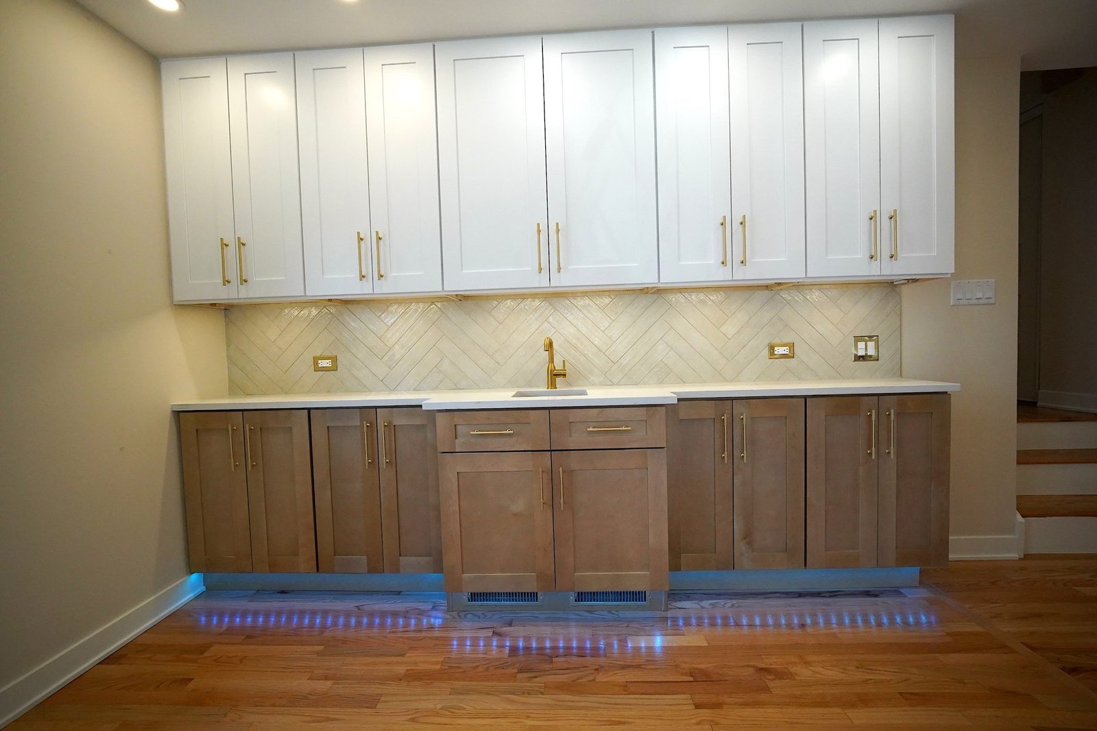 Wall of white upper cabinets with brass pulls and herringbone backsplash