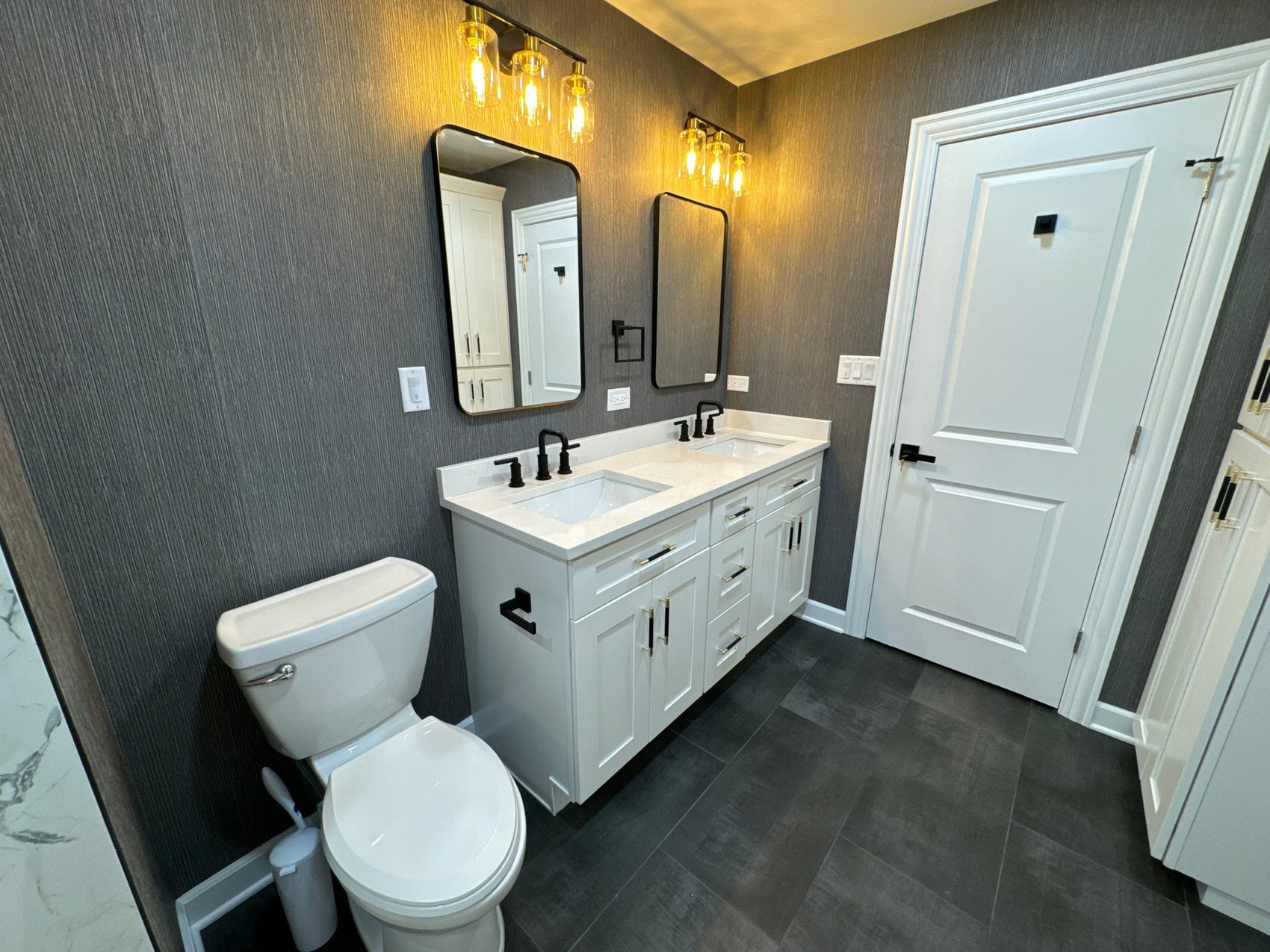 Remodeled bathroom with white double vanity, textured dark wall and black fixtures