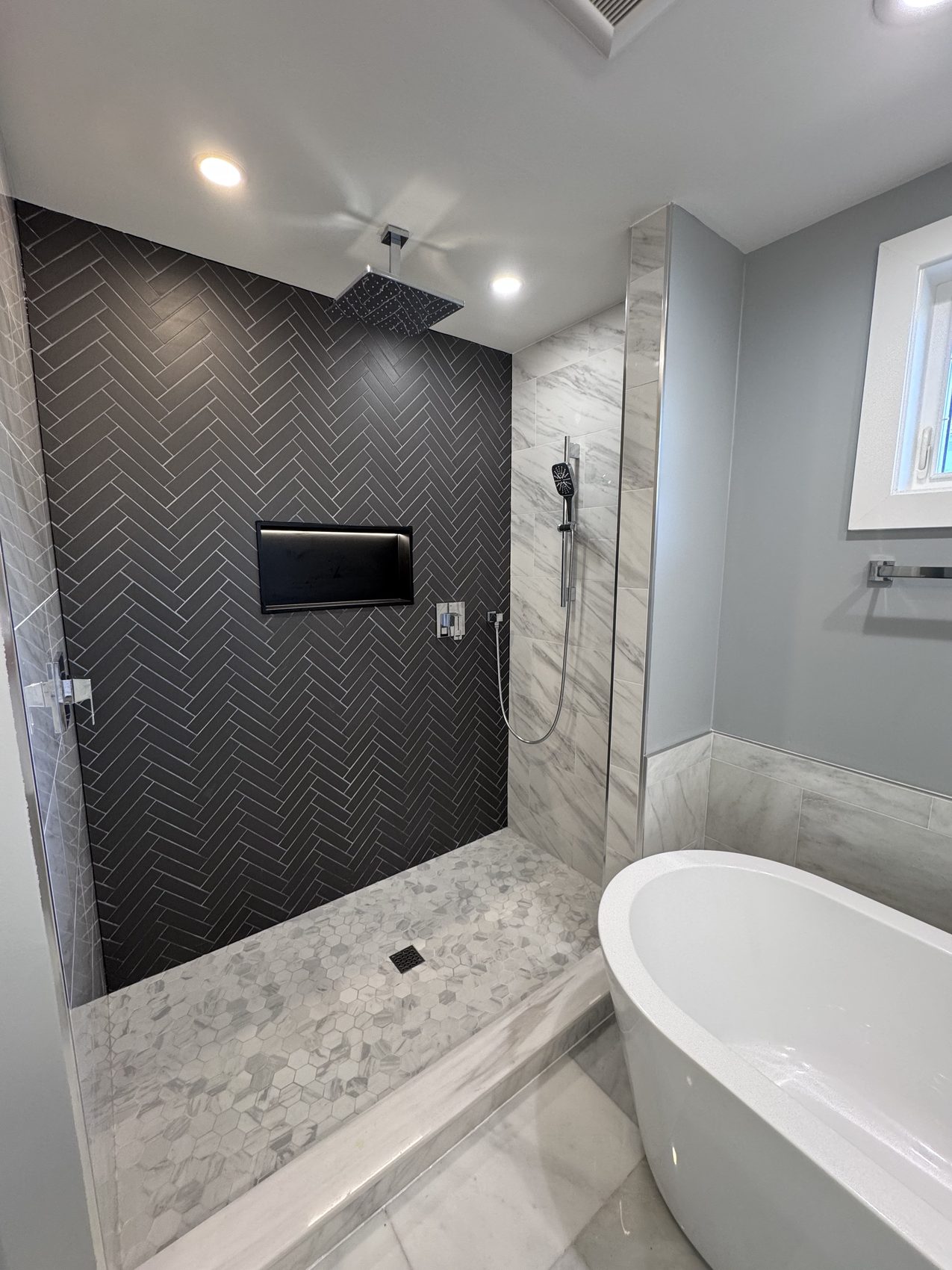 Remodeled bathroom with herringbone tile shower and freestanding tub