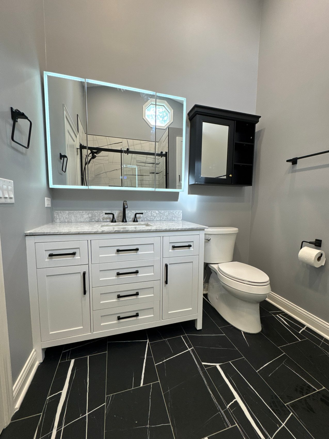 Remodeled bathroom with white vanity, black veined floor tile and LED mirror cabinet