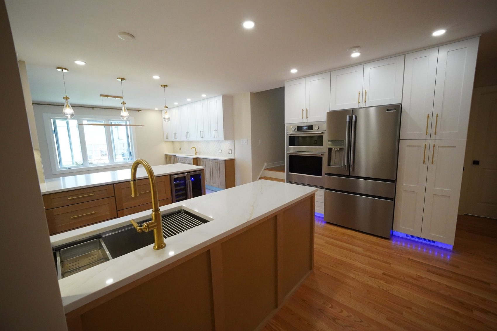 Remodeled kitchen with quartz island, brass faucet, wine fridge and tall white cabinets
