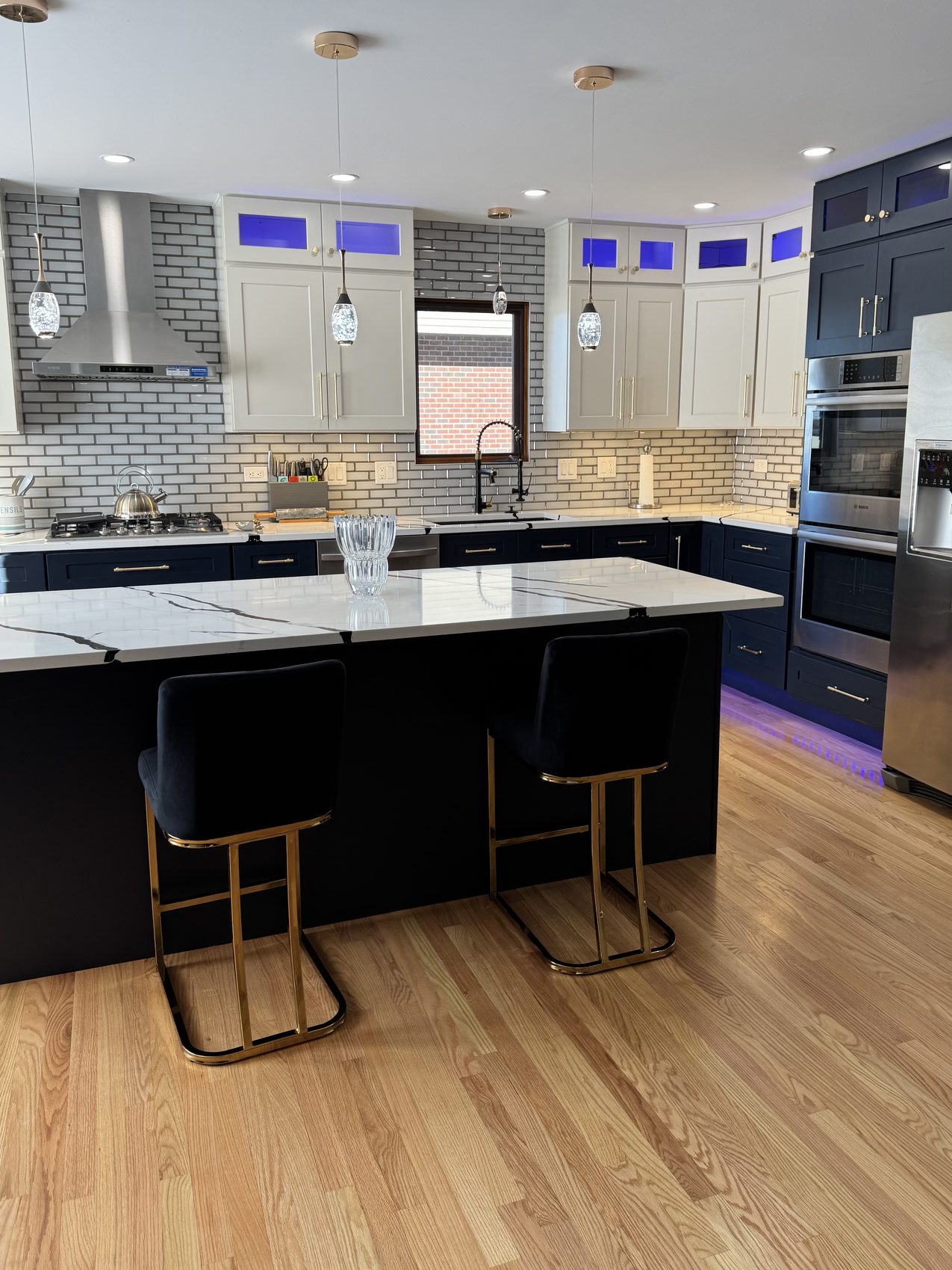 Remodeled kitchen with navy island, brass bar stools and white cabinets