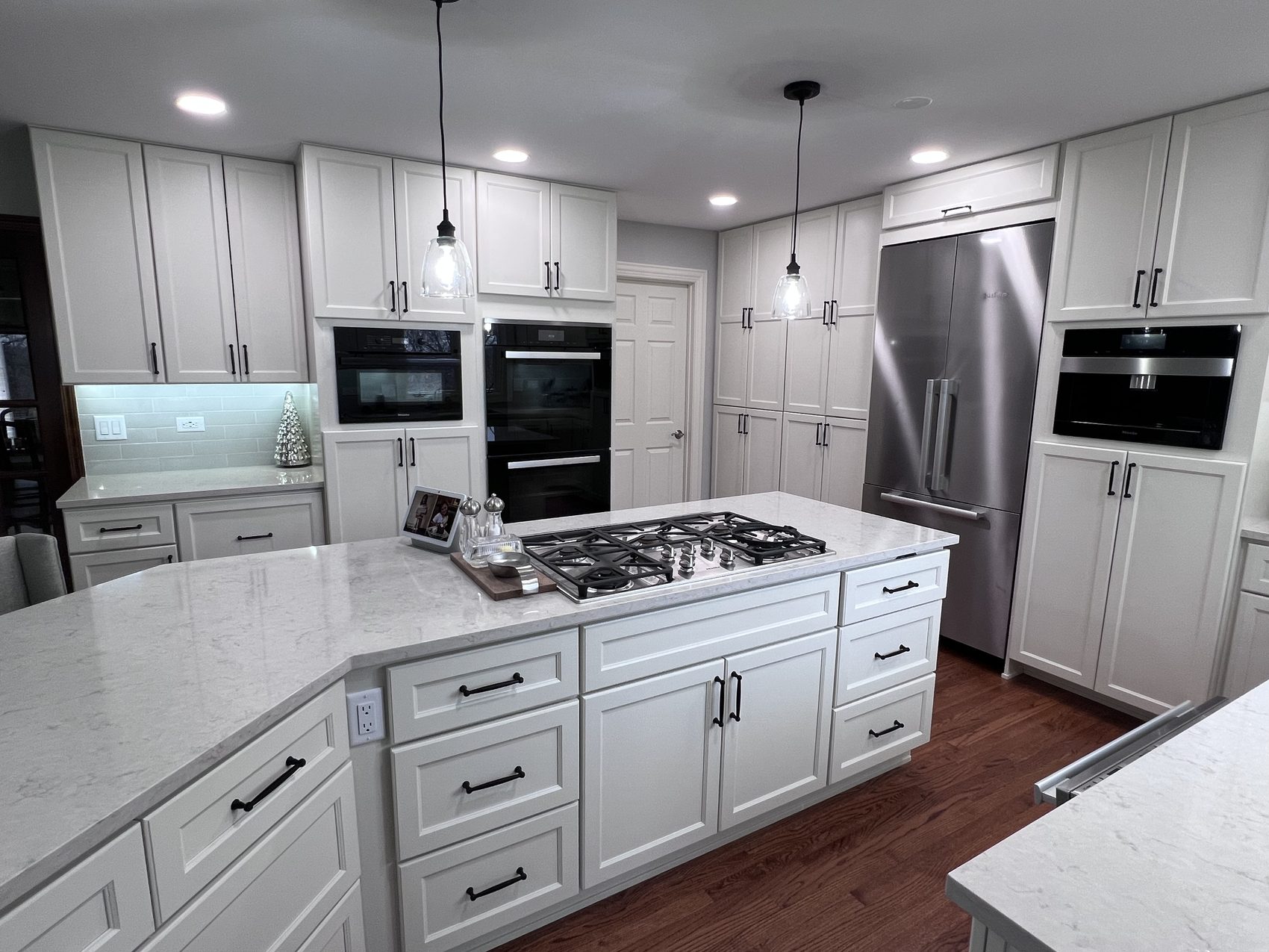 Remodeled white kitchen with cooktop island and built-in ovens