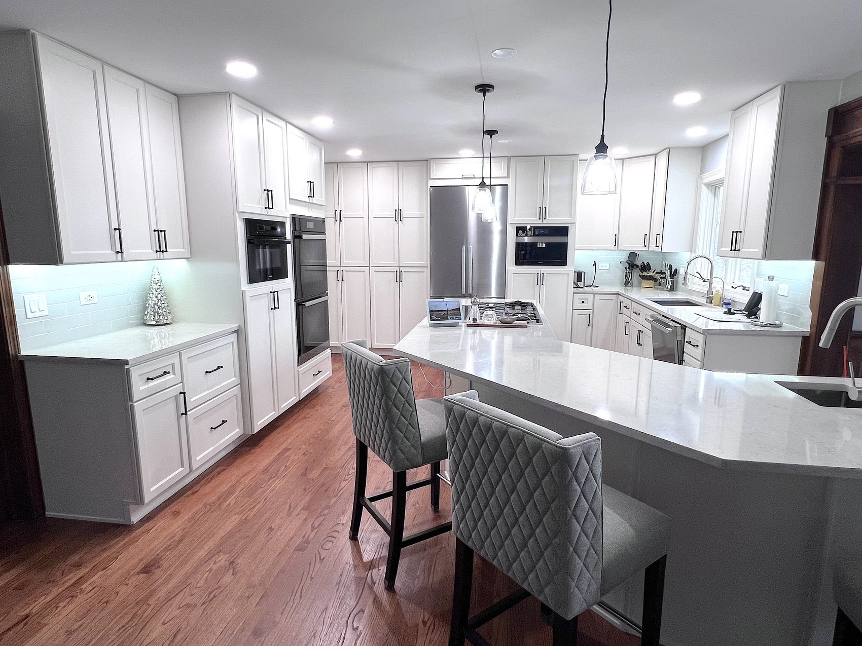 Remodeled white kitchen with a long quartz island and upholstered stools