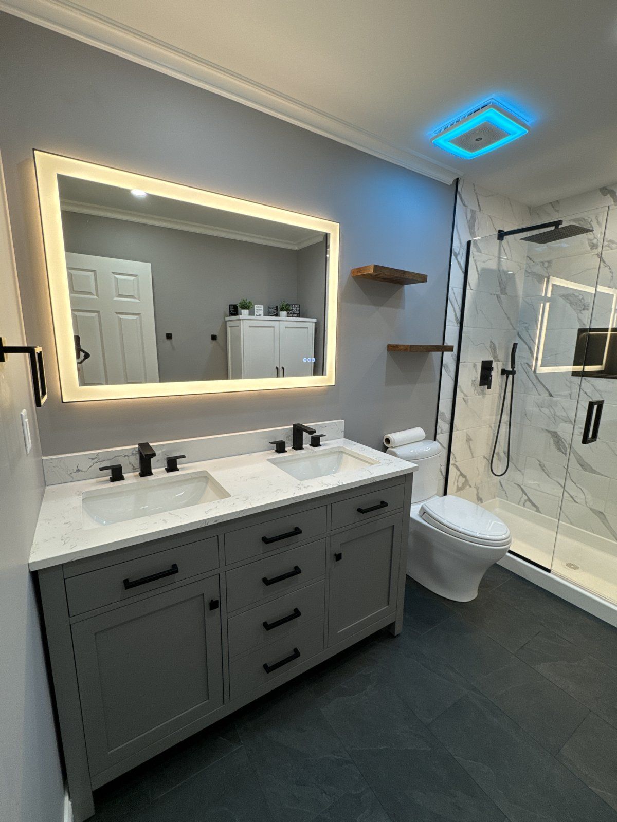 Bathroom with backlit mirror, marble-look glass shower and illuminated blue exhaust fan