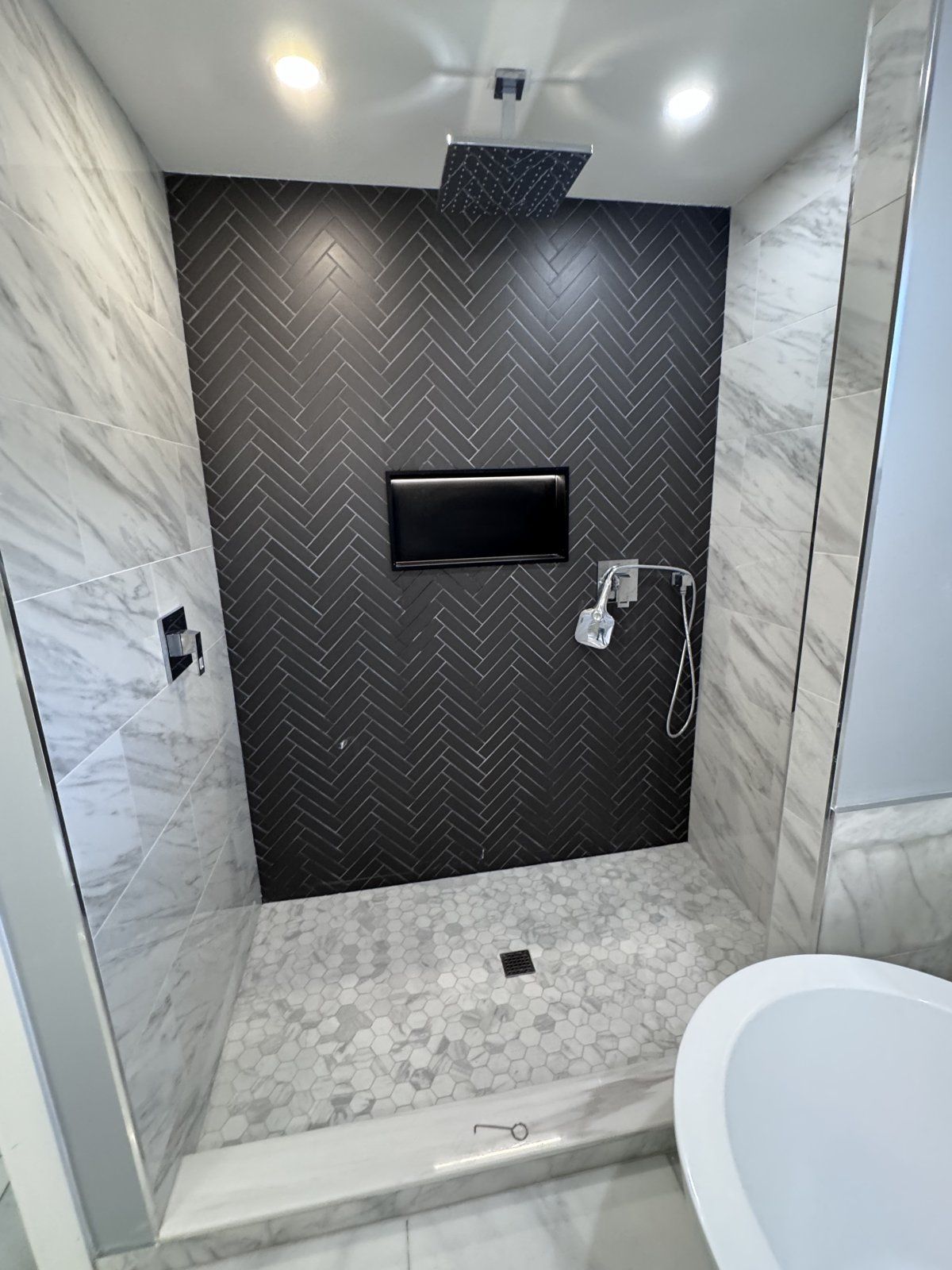 Walk-in shower with black herringbone accent wall, marble-look tile and hex mosaic floor