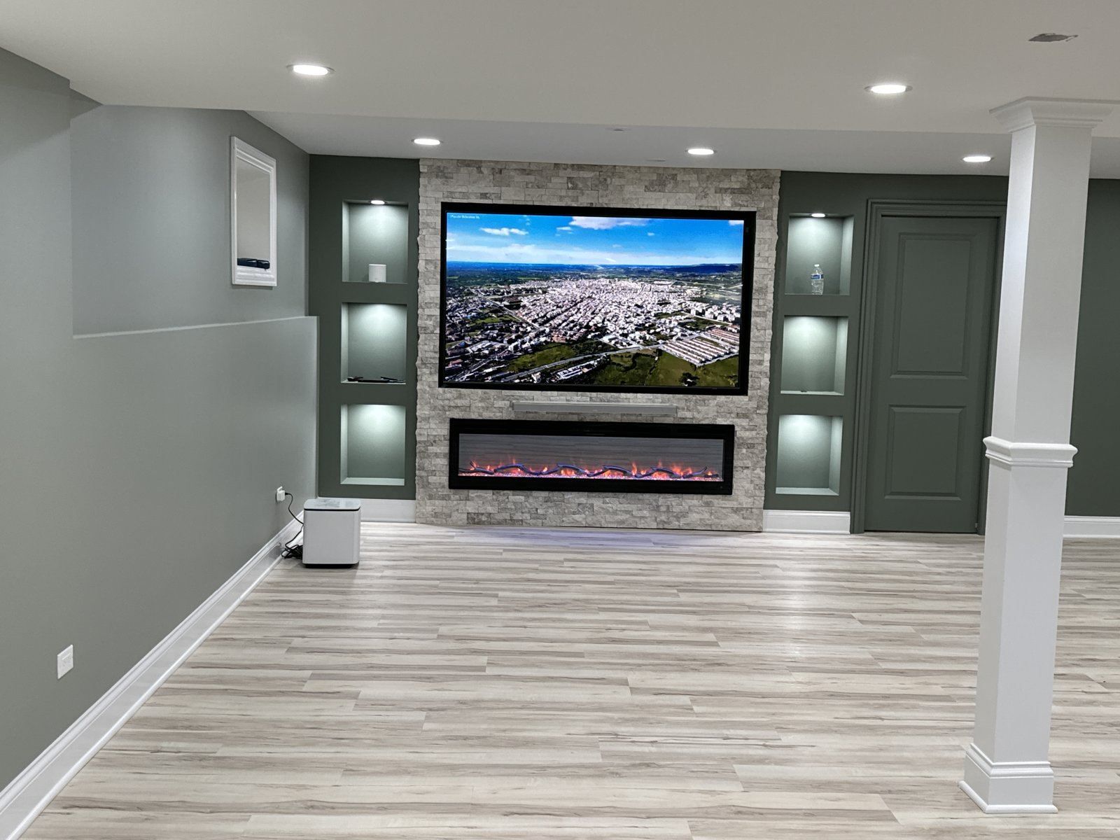 Finished basement media wall with large TV, lit niches, stone accent and linear fireplace