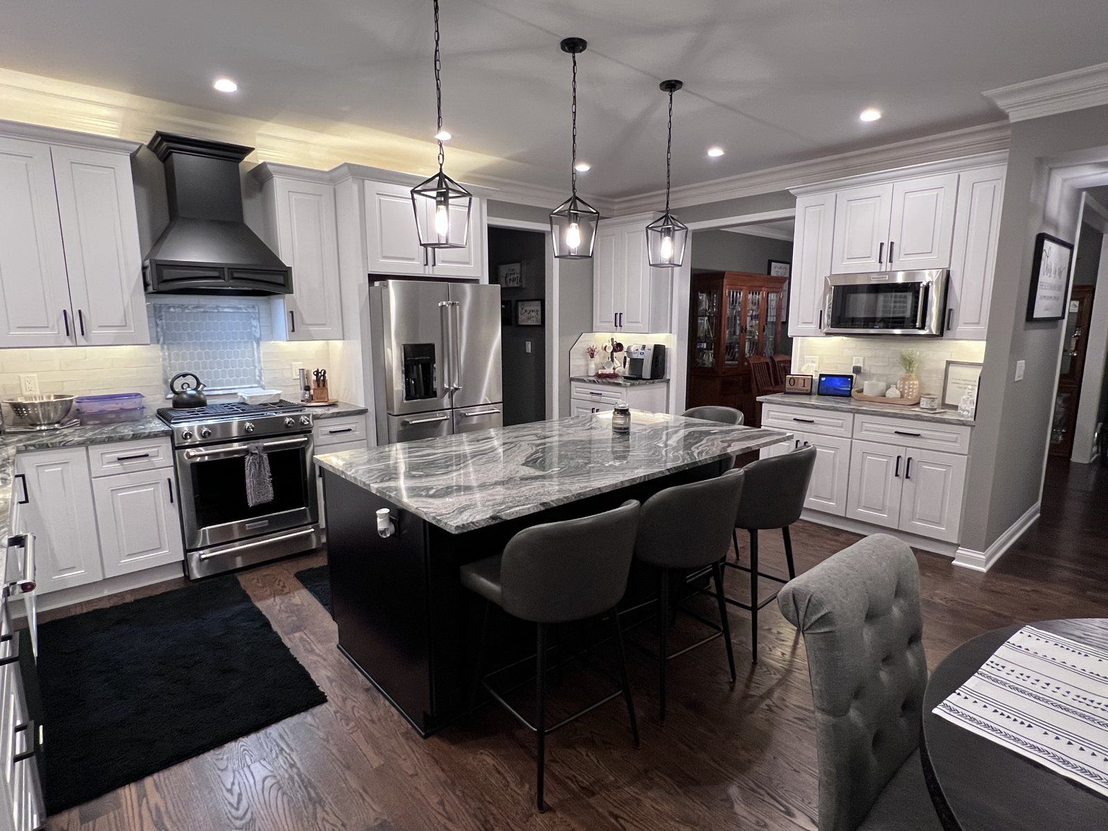 White kitchen with a black range hood, granite island and lantern pendants