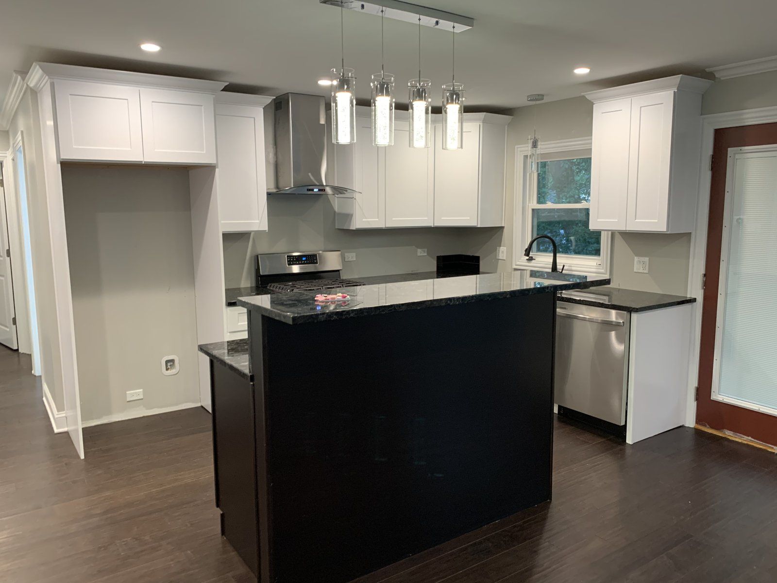 Bright white kitchen with a window, dark island and linear pendant lights