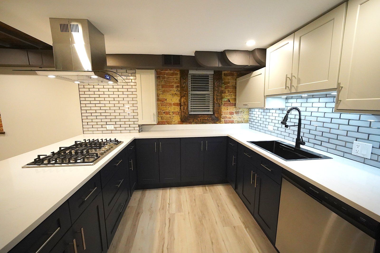Navy kitchen with gas cooktop, brick accent wall and subway tile backsplash