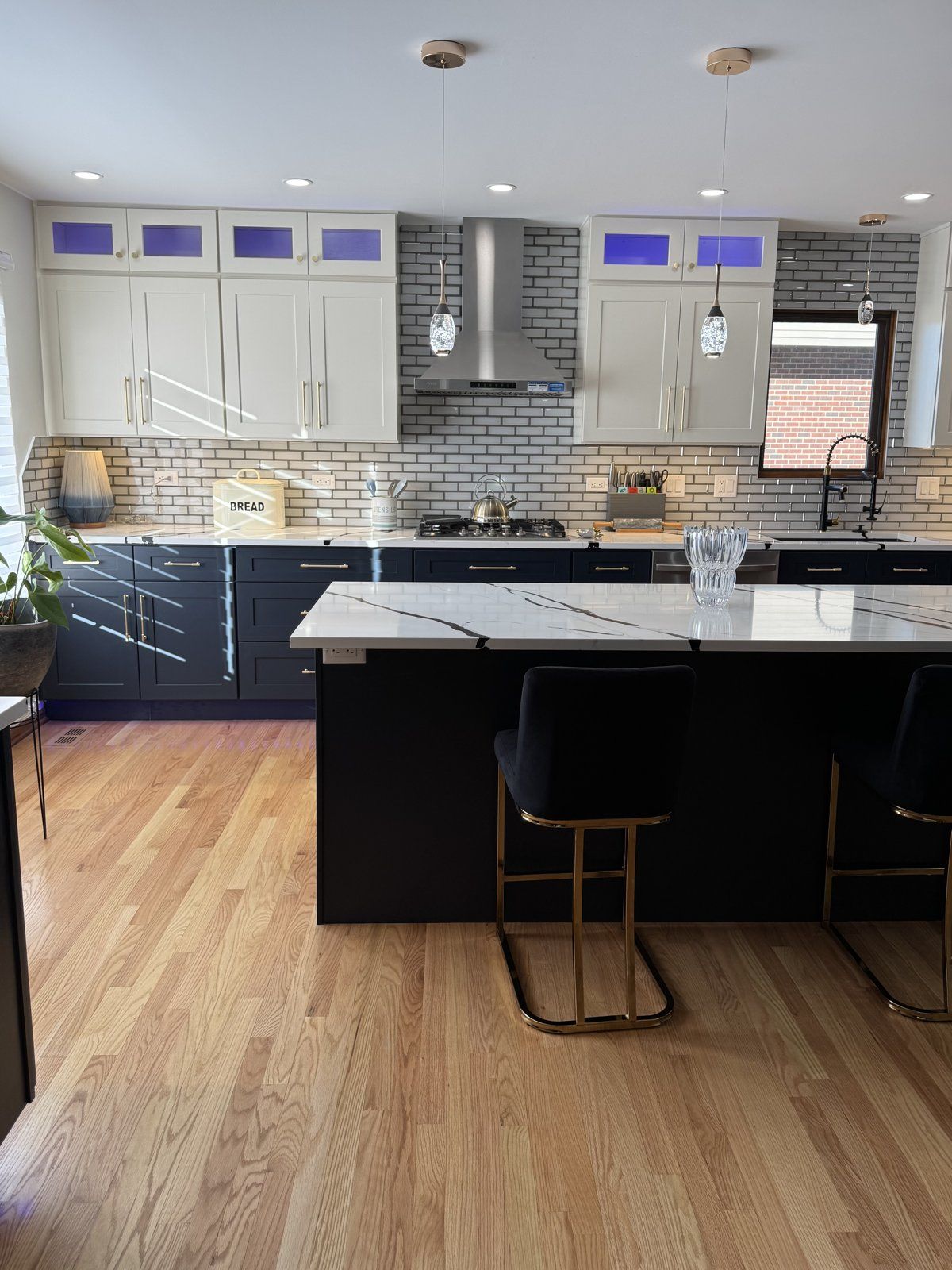 Navy island kitchen with marble-look quartz, brass stools and LED lighting